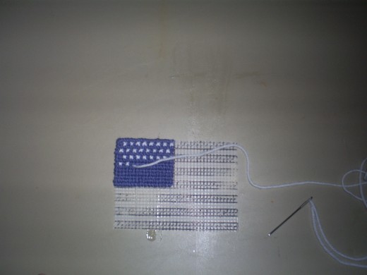 Continue cross stitching on all fifty white stars on the blue canton of the American flag.