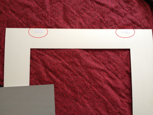 Step 3. Affix two small pieces of double-sided archival tape to the top of the matting as shown in this photograph. Peel off the top layer to expose the sticky topside of the tape.