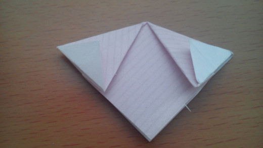 Fold the tips back, so the crease is in line with the diamond shape below.