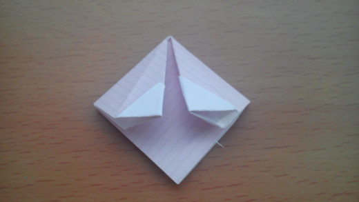 You should end up with a diamond like this. Dab some glue along one of these upper flaps, fold the diamond in half vertically so the flaps stick to each other.