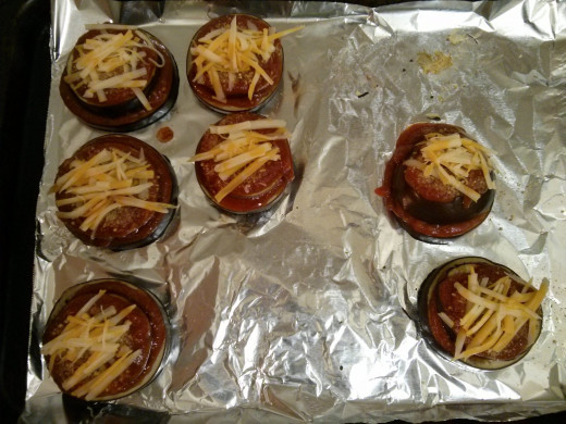 Covering the first layer of eggplant with a smaller piece, followed by tomato sauce and cheese