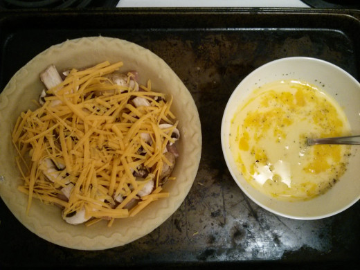 Pie crust with the dry ingredients added to it, while bowl to the right contains the milk and egg mixture, ready to be poured in to the crust too.
