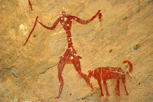 A prehistoric painting showing a human with a dog like animal.