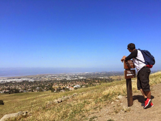 Halfway up the peak, a hiker takes a breather and enjoys the view of the valley along a trail marker.