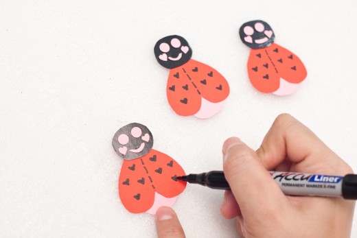Cut out shapes from the pink construction paper to make lips, eyes and dimples.  Use your Sharpie to make tiny hearts on the wings.