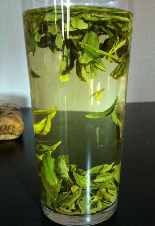 Loose leaf longjing tea brewed directly inside a drinking glass.