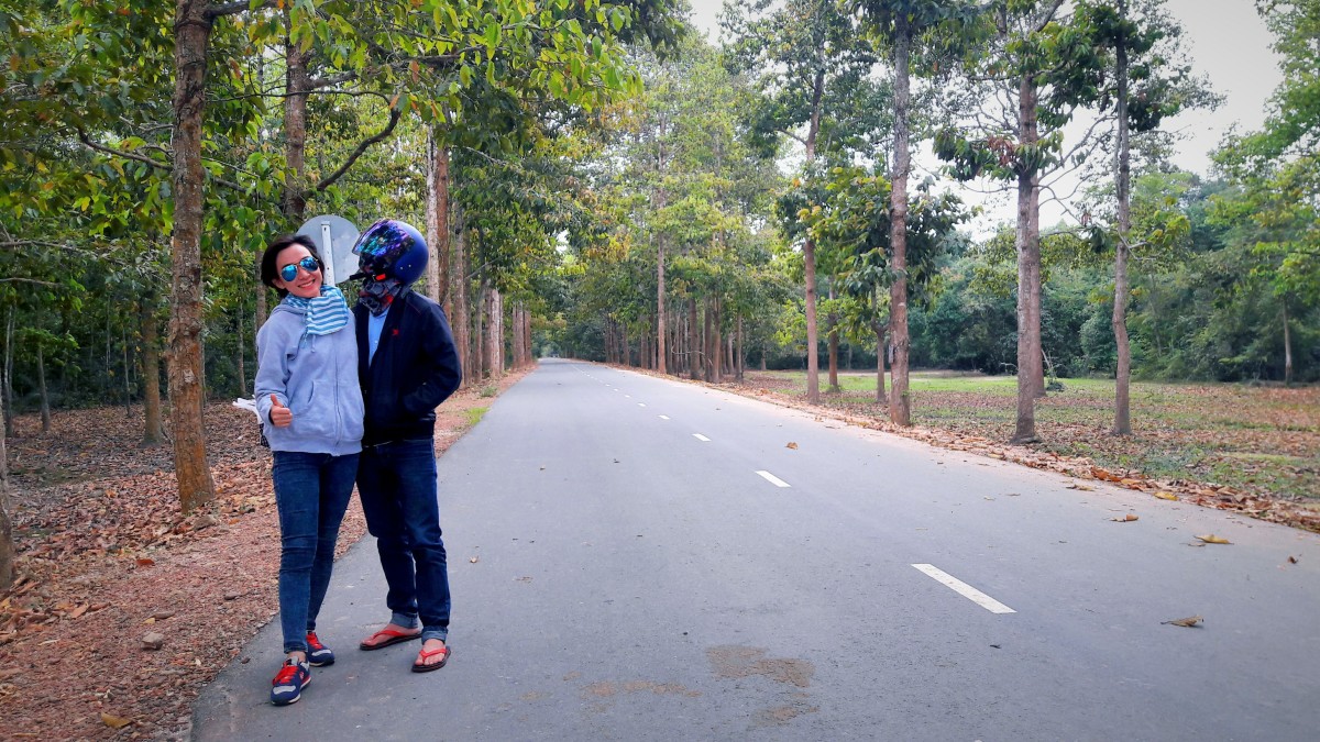 A couple posing on the road piercing the lush green forest.