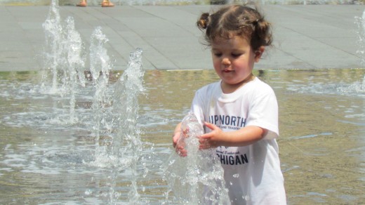 This young child was immersed in the water from the fountain as her parents looked on.