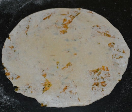 Place the raw paratha on a hot pan. Sprinkle ghee and oil mixture on it.