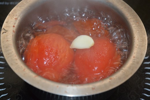 Step two: Boil the tomatoes in water. Add garlic cloves to it.