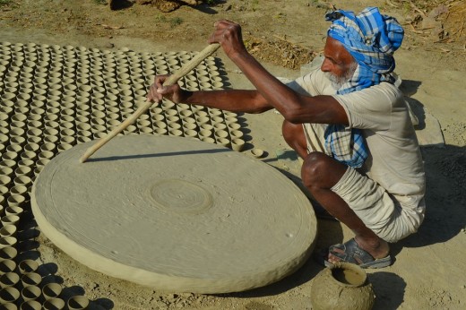 Old man turning the wheel for giving shape to potteries