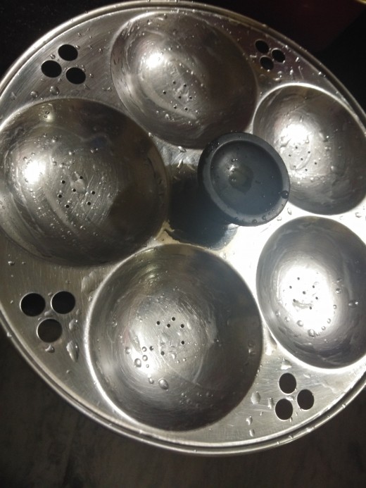 Grease idli stand with oil. Add water to the steamer and heat it.
