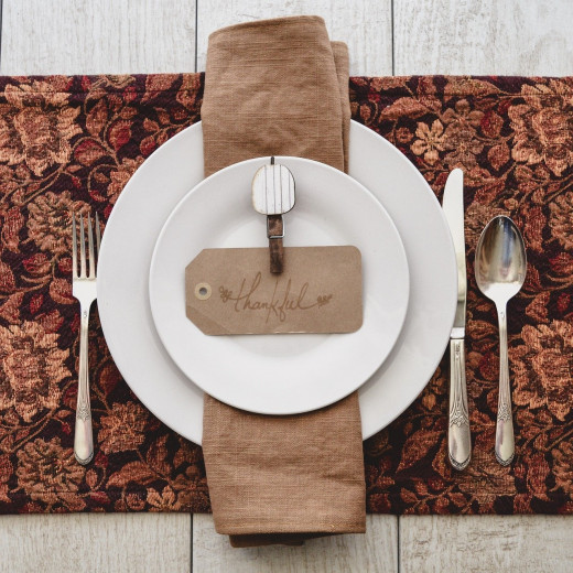 The rich burgundy and rust colors in the placemat set off the white plates. Here, they are accented by a tan napkin and namecard. A rustic clothespin with a white pumpkin attached complete the theme.
