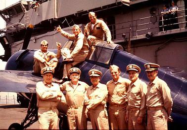 Some cast members of Midway, 1976, pose on the USS Lexington in front of an F4F Wildcat.