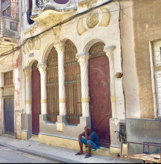 A man resting on the doorstep of a Baroque building which still has conserved its beauty.