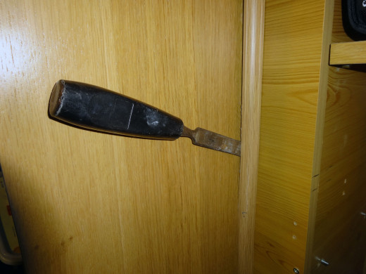 Using an old chisel to prise off the decorative corner moulding next to the shelving unit, so as to fit the recycled doorframe .