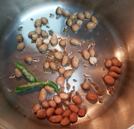In a pan, heat 1-2 teaspoons of cooking oil. Splutter 1/2 teaspoon of cumin seeds, 1-2 tablespoons of peanuts and 1-2 split green chilies. Fry till peanuts turn golden brown and crisp.