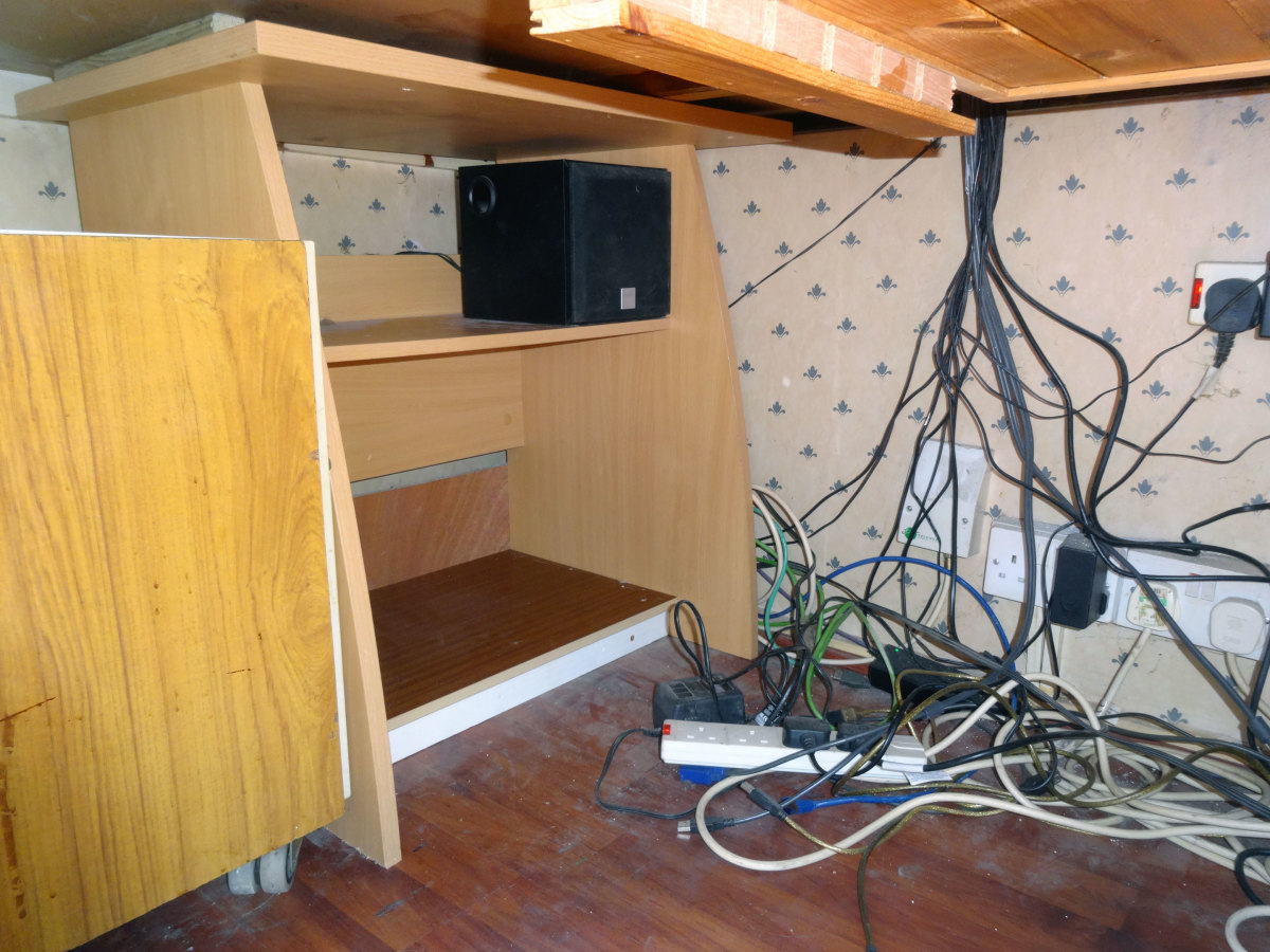 The old Ikea desk relocated to the corner beneath the main desk, and base speaker wired up on the top shelf