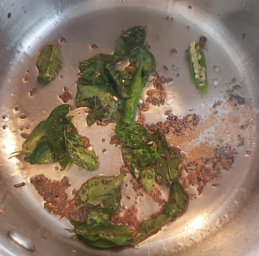 Add 1-2 strings of fresh curry leaves, 1/4 teaspoon of hing or asafoetida and 1-2 split or chopped green chilies (adjust as per taste). Fry fro a minute.