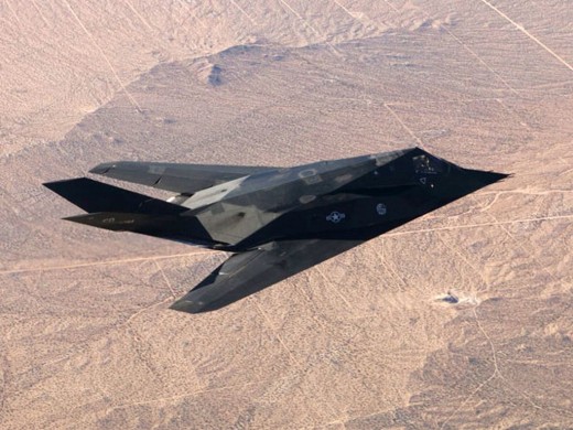 a F-117 Nighthawk stealth fighter seen from above as it flies in daylight over a desert.