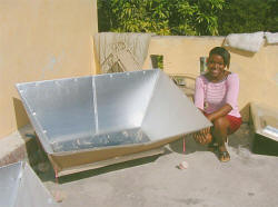 A woman in Haiti tests a solar oven which cooks food, pasteurizes water, and eliminates the need for charcoal, about 55% of a family's income. Haiti has only 2% of its original forests remaining--the rest of the land is bare and subject to erosion.