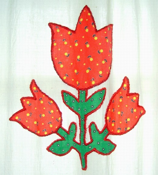 CLOSE UP OF FLOWER CUT OUT OF FABRIC, WITH THE BORDER SEWN ON USING RED EMBROIDERY FLOSS