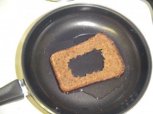 Oil is added to the frying pan and a bread slice is added. The bread will absorb some of the oil.  Bread slices must be perfectly horizontal, else the egg will leak out