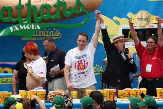 Image from 2008 Nathan's Hot Dog Eating Contest. Joey Chestnut is the middle being declared the winner by event organizer George Shea. Walking away in the red hair is Takeru Kobayashi, six time winner of the contest.