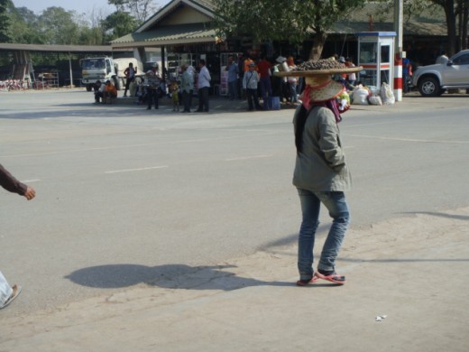 Lady carrying shells to eat on wicker tray on her head.
