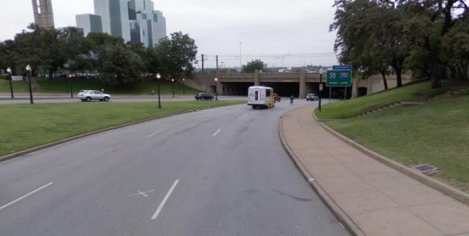 Dealey Plaza looking toward the underpass. The grassy knoll goes up on the right side next to the sign. The white "X" on the left side indicates the location of the President when he was shot