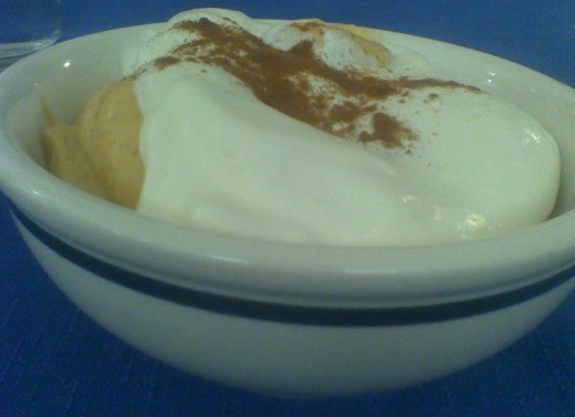 A small bowl of pumpkin mousse dessert, topped with a dollop of  whipped cream and a sprinkling of ground cinnamon
