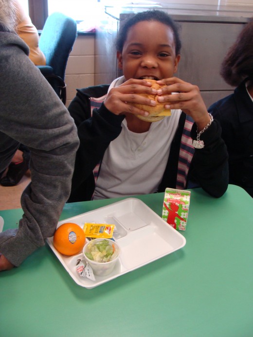 This student's lunch was a mix of high and low quality food.  The processed hamburger was served on what appeared to be a whole wheat bun and lettuce, with an orange and strawberry flavored milk.
