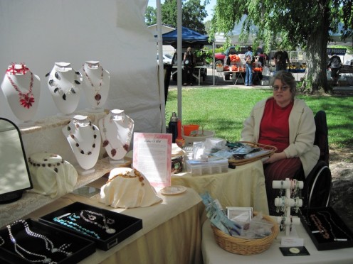 Aileen sits in her booth with the tools of her trade in front of her and the results of using those tools and materials all through the booth. 