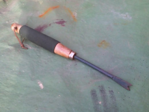 This tool is a weed poker. It has a small wooden handle and a long metal bar with a flatten v shape at the tip. 