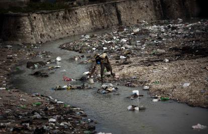 A man collects water in a river covered with waste in Port-au-Prince, Haiti, on Friday. AP photo