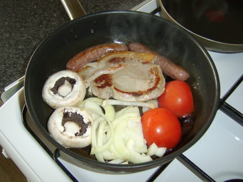 The tomato, mushrooms and onion are added to the partially cooked pork and sausages
