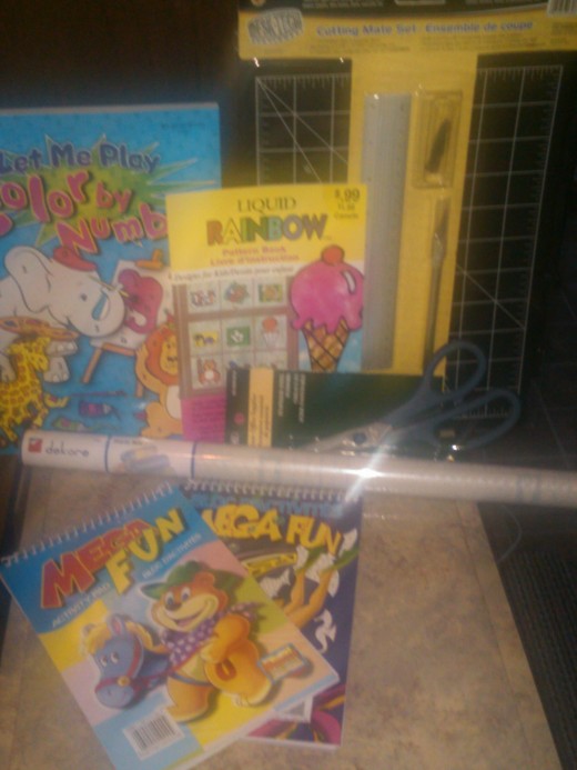 Left,middle, and front, shows different kinds of books that can be used to choose your picture from. Right; cutting mat set with a ruler and exact o knife with blades. In front right; scissors, and middle front; clear adhesive. 