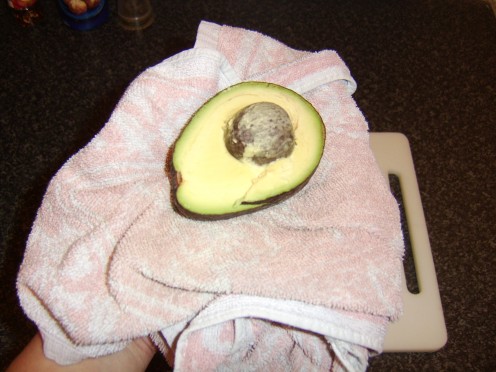 Place a thick folded towel on the palm of your weaker hand and the half of the avocado containing the stone on top