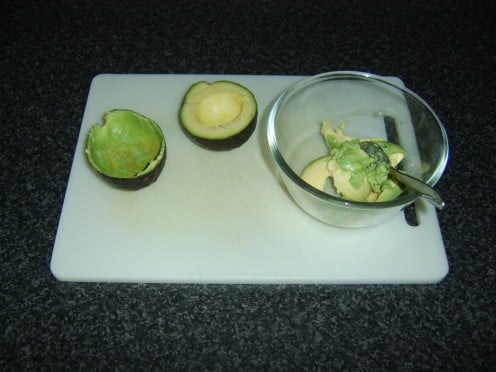 The flesh is carefully scooped out of the avocado halves with a teaspoon