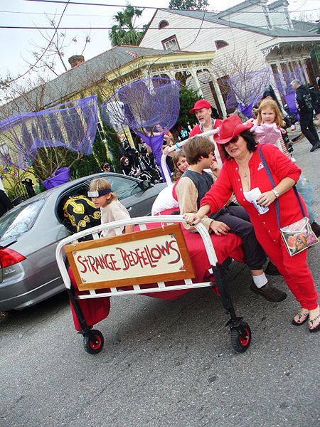 "Strange Bedfellows". New Orleans Mardi Gras revelers pushing bed in neighborhood street