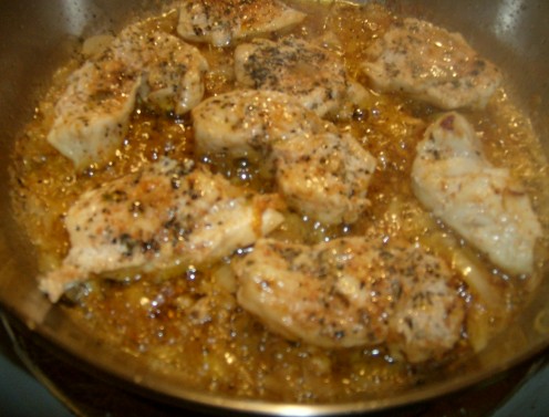 Chicken breast pieces browing with herbs and other seasonings.