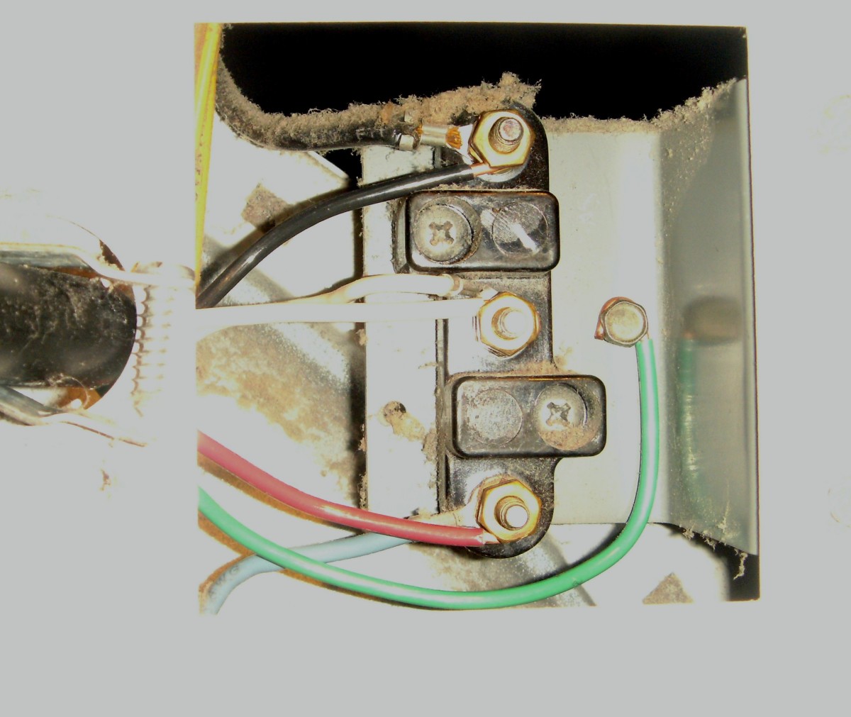 The four-pronged cord has been loosened from the dryer wall and is ready to be disconnected from the terminals.  Pay particular attention to where the white and green wires go.
