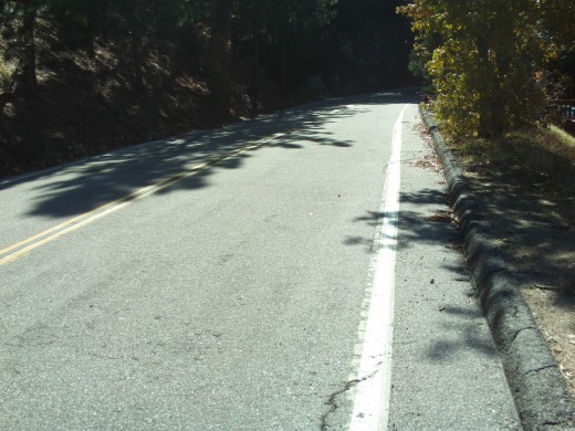Looking down a steep road in the San Bernardino Mountains.  There are trees to be seen on both sides of the road.