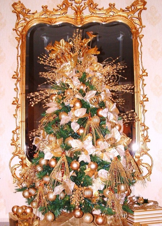 Elegant gold themed tree was displayed on a mahogany table with guilded mirror behind it.