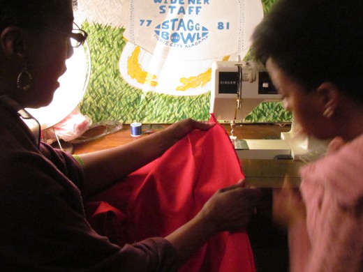 Karen instructs Jaleesa on sewing the pair of red pants she wants to design.
