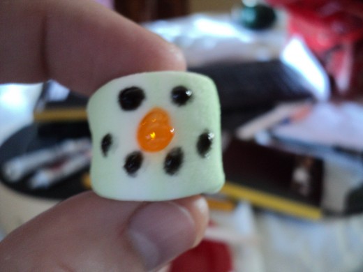 Use black gel frosting to make two eyes and a mouth on the small marshmallow.  Use orange frosting to make a carrot nose.