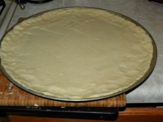 Pressed out to the edges by hand. Insure you brush edges & lightly brush the entire crust with olive oil. Baking the dough for 7 minutes keeps the sauce from soaking in.