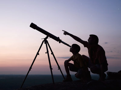 A father and son peer at the sky through a telescope