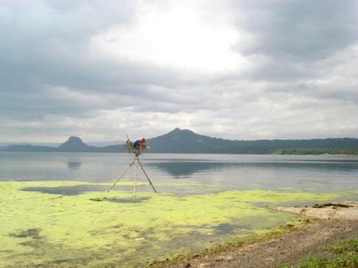 a local sitting on top of a makeshift stickstand shooting some fish at the Lake Taal, Volcano overhead...