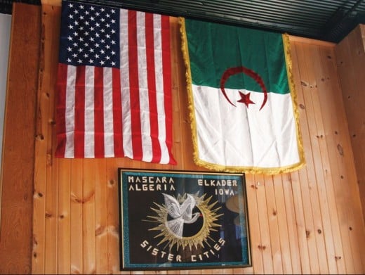 American and Algerian flags hang on the wall of Sheha’s Cafe in Elkader, Iowa, above artwork celebrating the sister-city relationship between Elkader and Abd el-Kader’s birthplace: Mascara, Algeria.